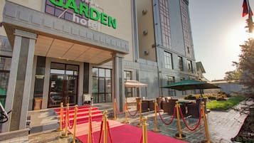 A hotel entrance with a red carpet, a sign reading 'GARDEN hotel,' and a flagpole with a flag.