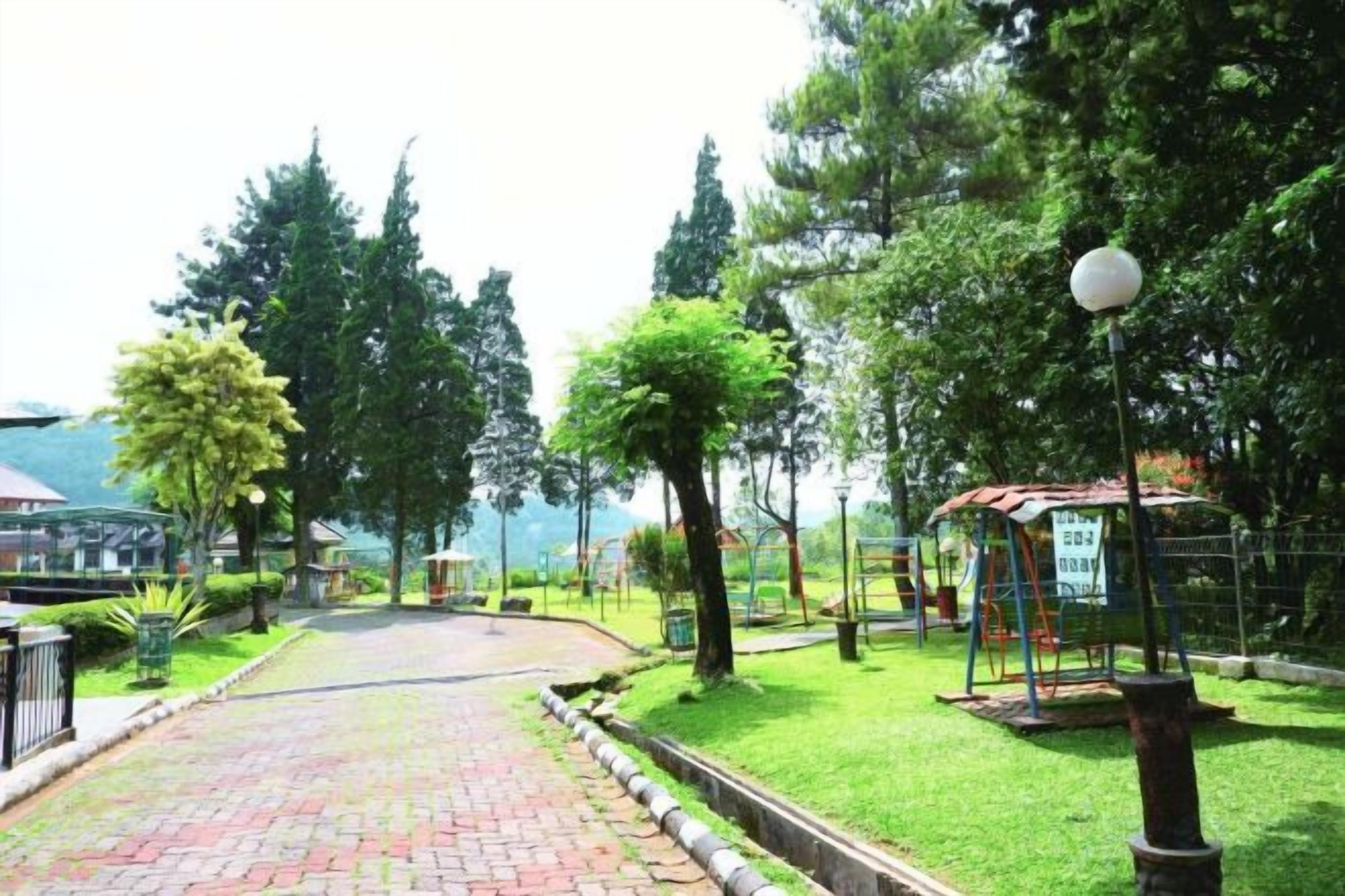 Un camino pavimentado que lleva a un parque infantil con columpios y un pabellón.