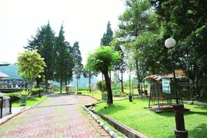 A paved pathway leading to a playground with a swing set and a gazebo. - Sanggabuana Puncak Convention & Resort (Pacet)