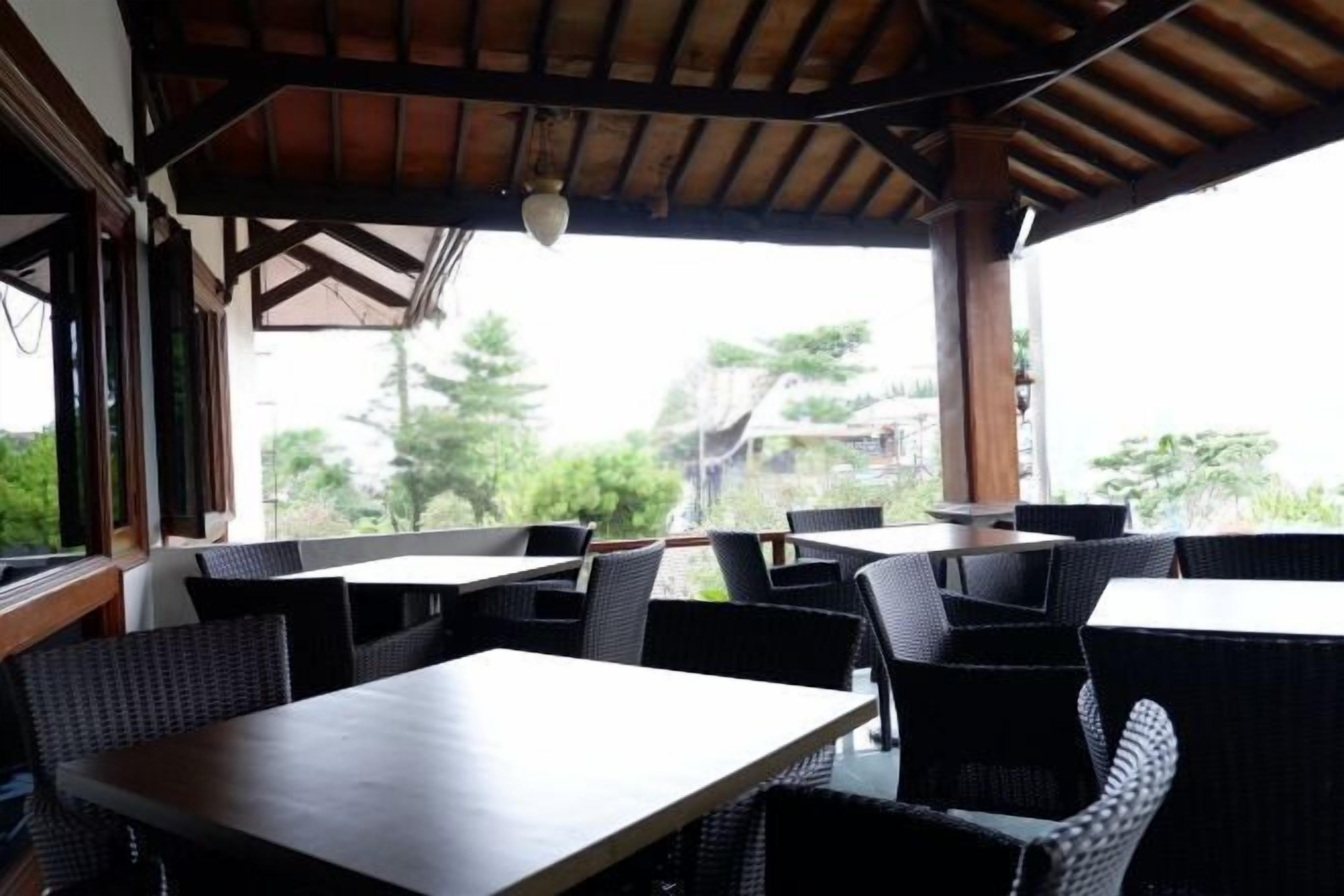 Un espace de restauration en plein air avec des tables et des chaises, un plafond en bois et une vue sur la verdure et les bâtiments.