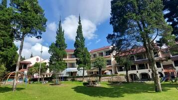 A courtyard with a grassy area, trees, and a building with multiple balconies and a red roof.