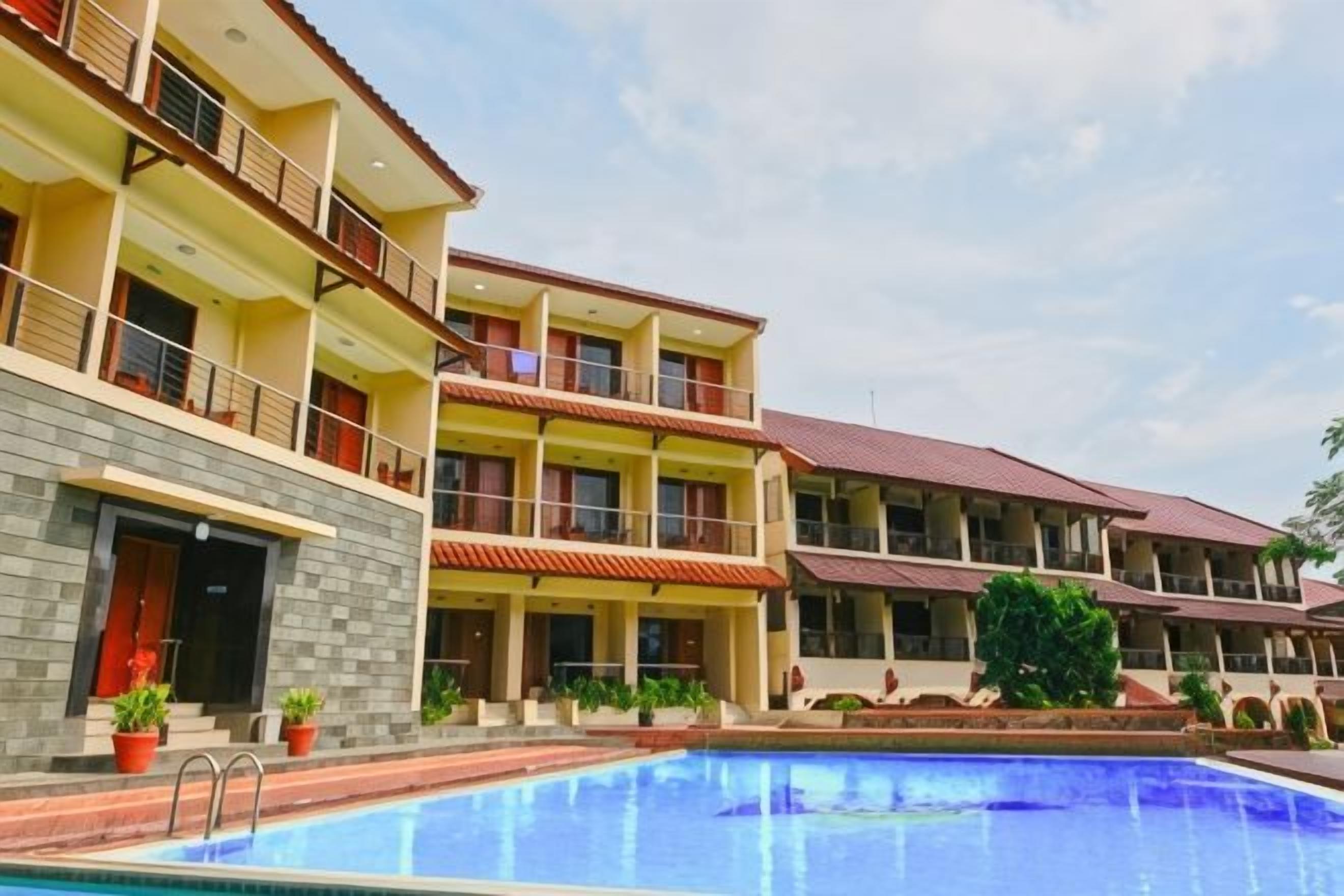 A hotel with multiple balconies, a swimming pool, and a clear sky.