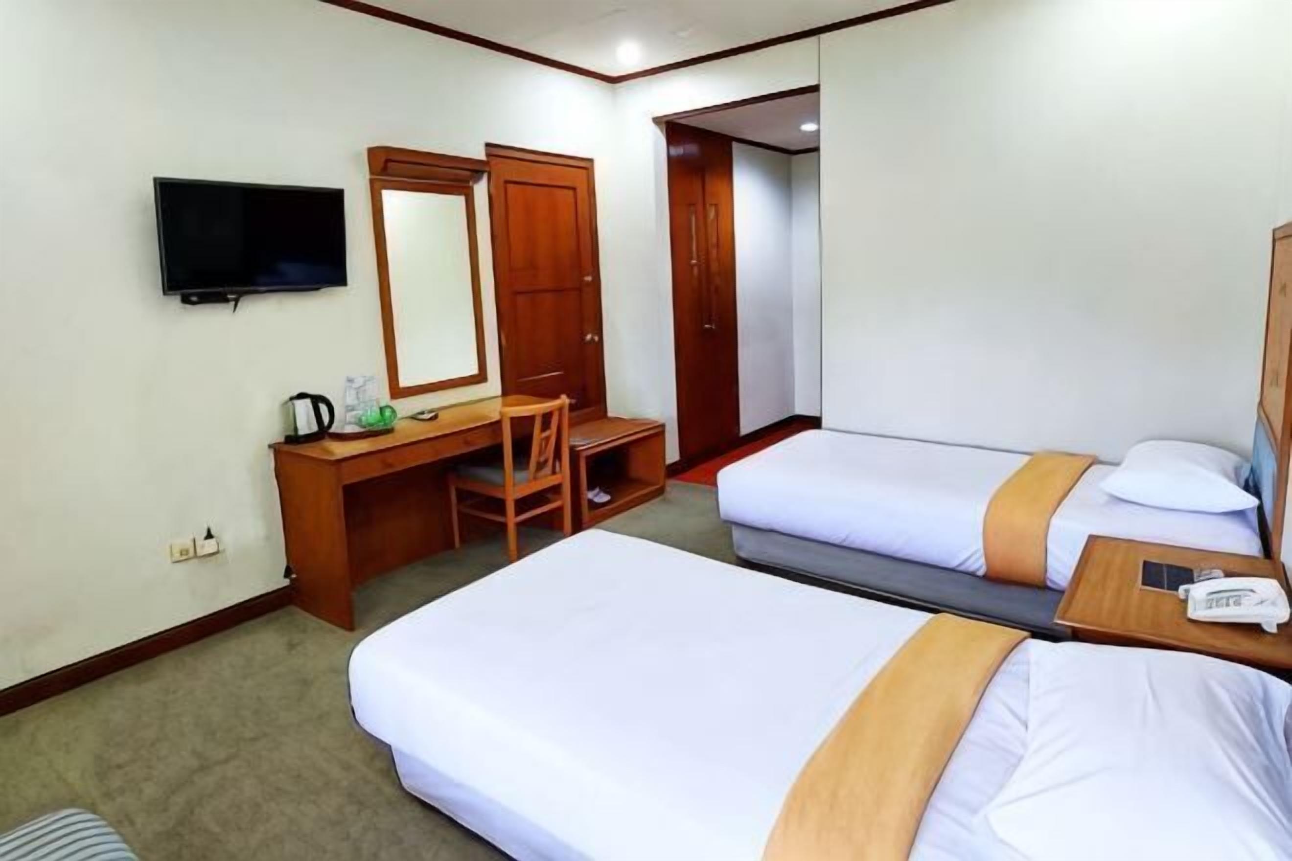 A hotel room with two beds, a desk with a chair, a television, and a mirror.