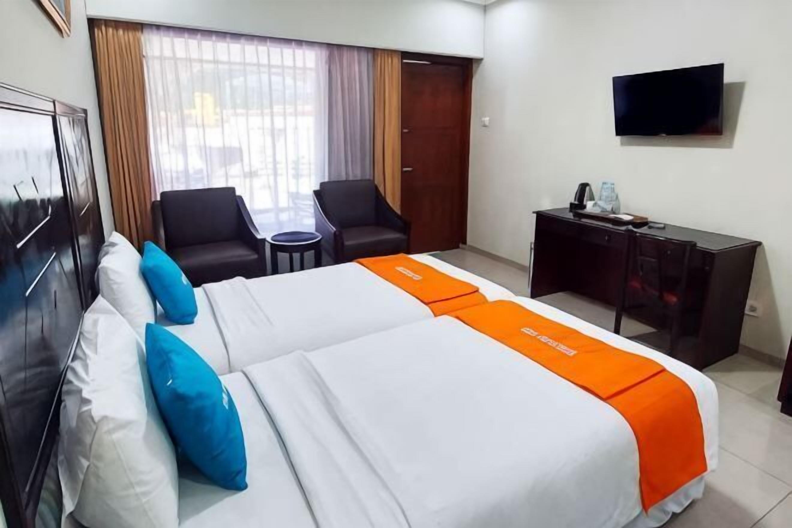 A hotel room with a bed, two chairs, a desk, a television, and a window with curtains.