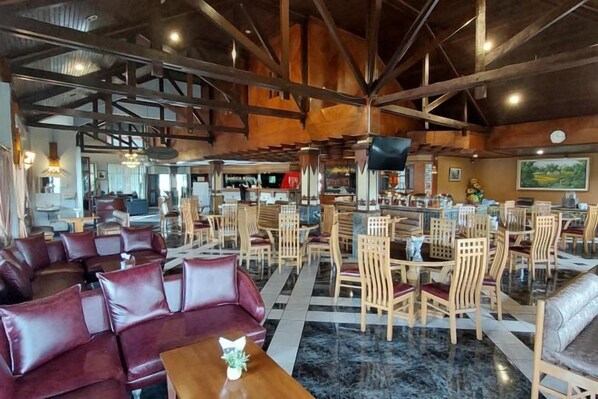 A spacious indoor area with multiple seating arrangements, including sofas and tables, and a bar area with chairs. - Sanggabuana Puncak Convention & Resort (Pacet)