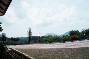 A paved outdoor area with a fountain, trees, and a mountain in the background. - Sanggabuana Puncak Convention & Resort (Pacet)