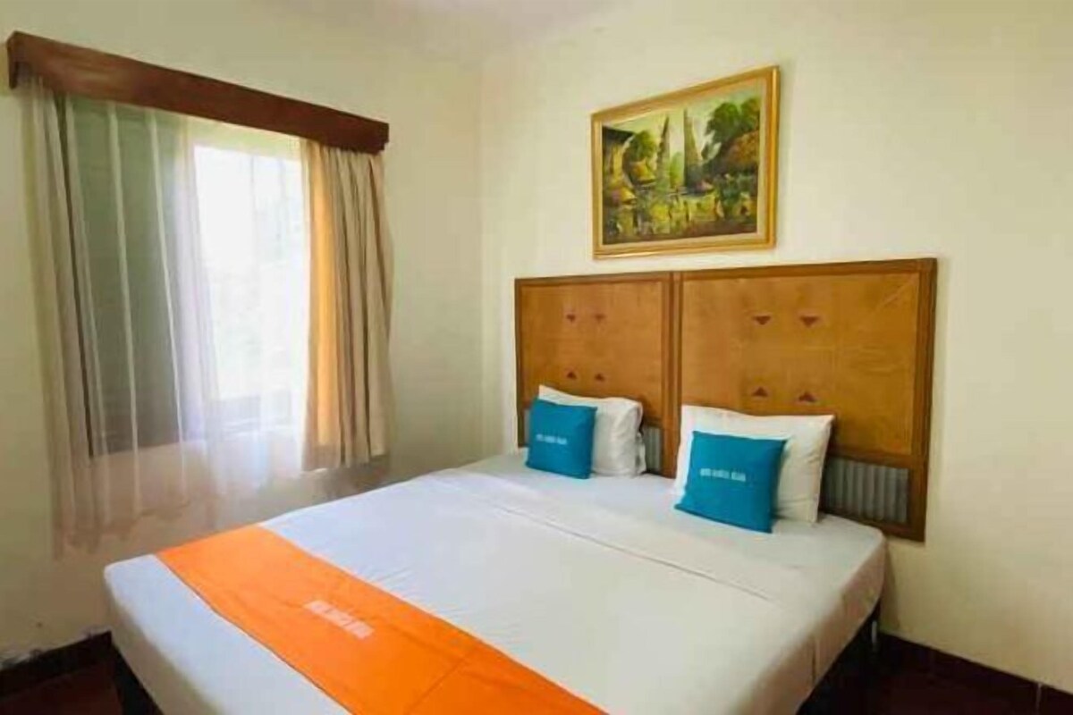 A hotel room with a bed, curtains, a painting, and a window.