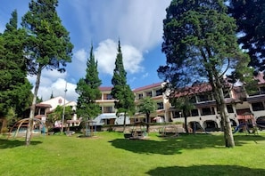 A courtyard with trees, a playground, and a building with multiple balconies. - Sanggabuana Puncak Convention & Resort (Pacet)