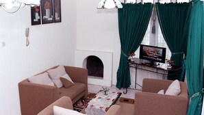 A living room with a sofa, armchair, and a television on a stand. - Hotel Ciloto Indah Permai (Cipanas)