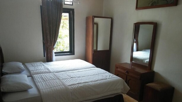 A bedroom with a bed, a wooden wardrobe, a mirror, and a window with curtains. - Hotel Ciloto Indah Permai (Cipanas)