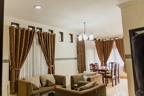 Habitación de hotel con sofá, mesa de comedor y cortinas.
