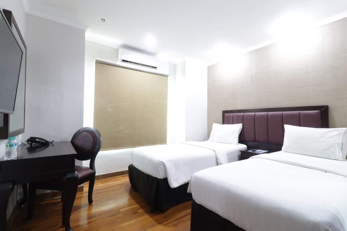 A hotel room with two beds, a desk, a chair, and an air conditioning unit.