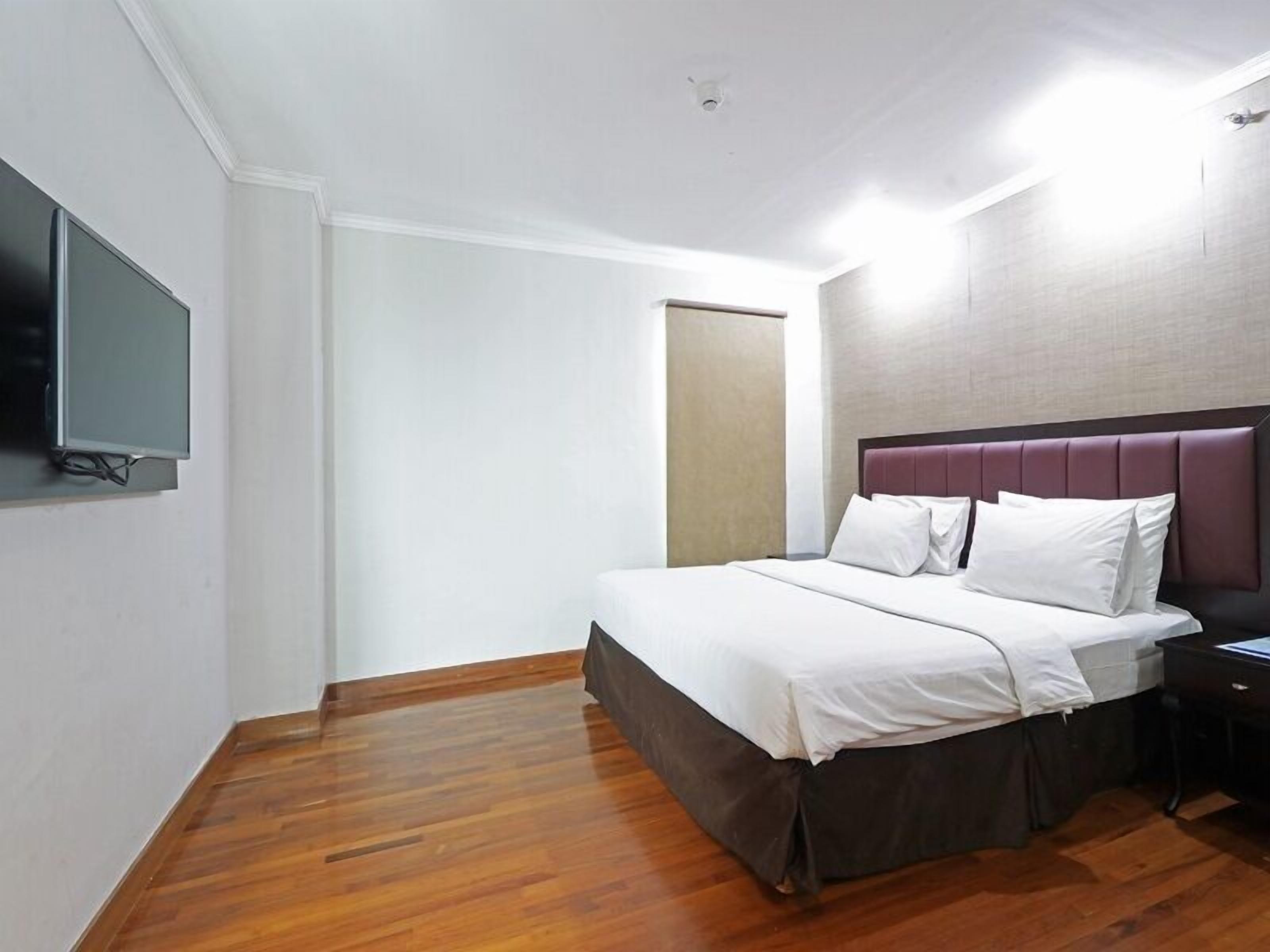 Habitación de hotel con cama, televisor de pantalla plana montado en la pared, suelo de madera y puerta que da a otra habitación.