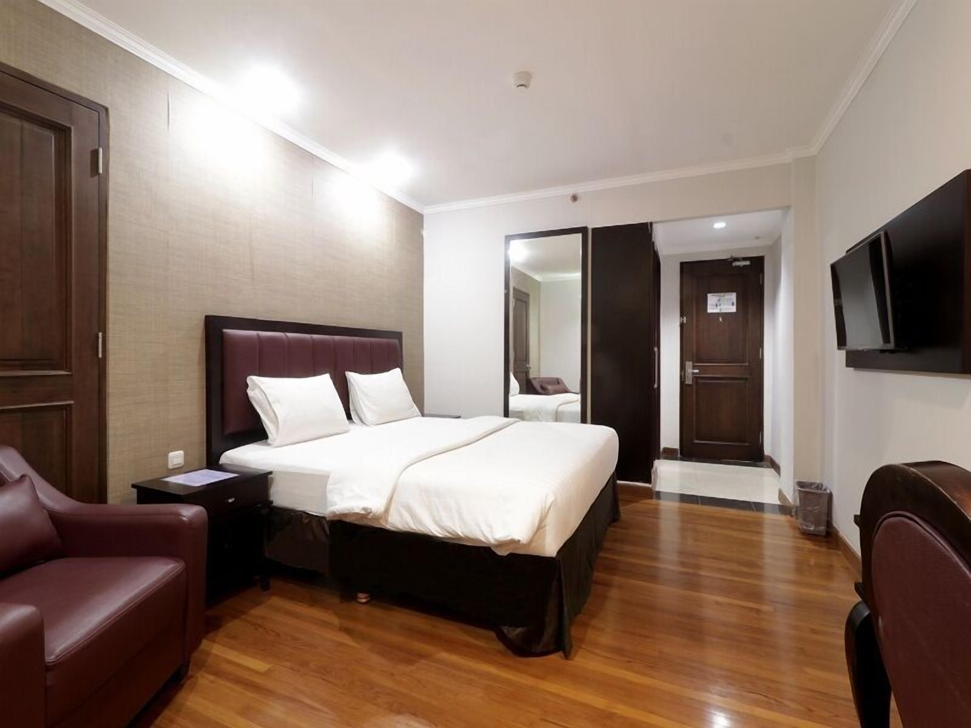 A hotel room with a large bed, a wooden floor, a TV mounted on the wall, and a door leading to another room.