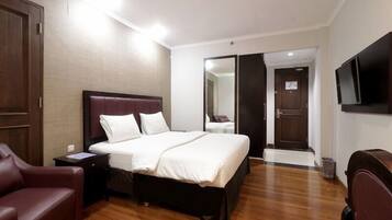 A hotel room with a large bed, a wooden floor, a TV mounted on the wall, and a door leading to another room.