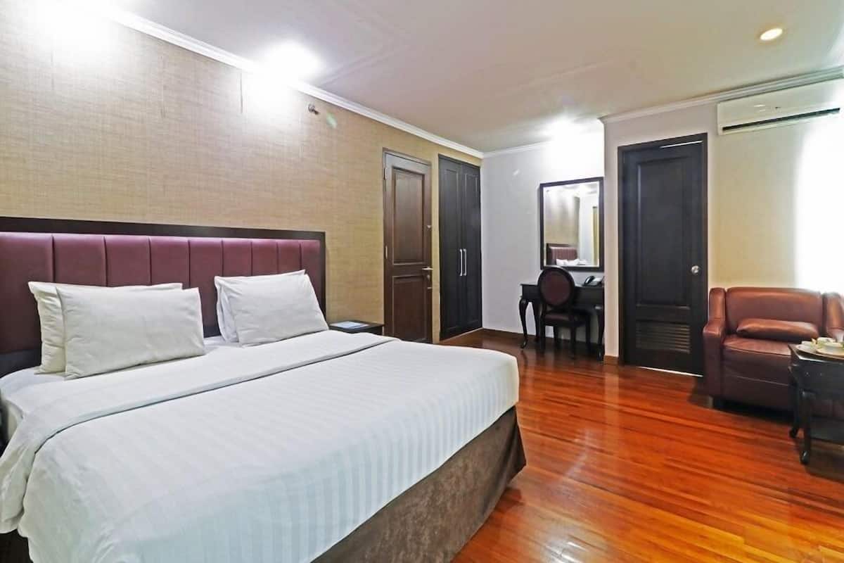 A hotel room with a large bed, a desk, a chair, and a sofa.