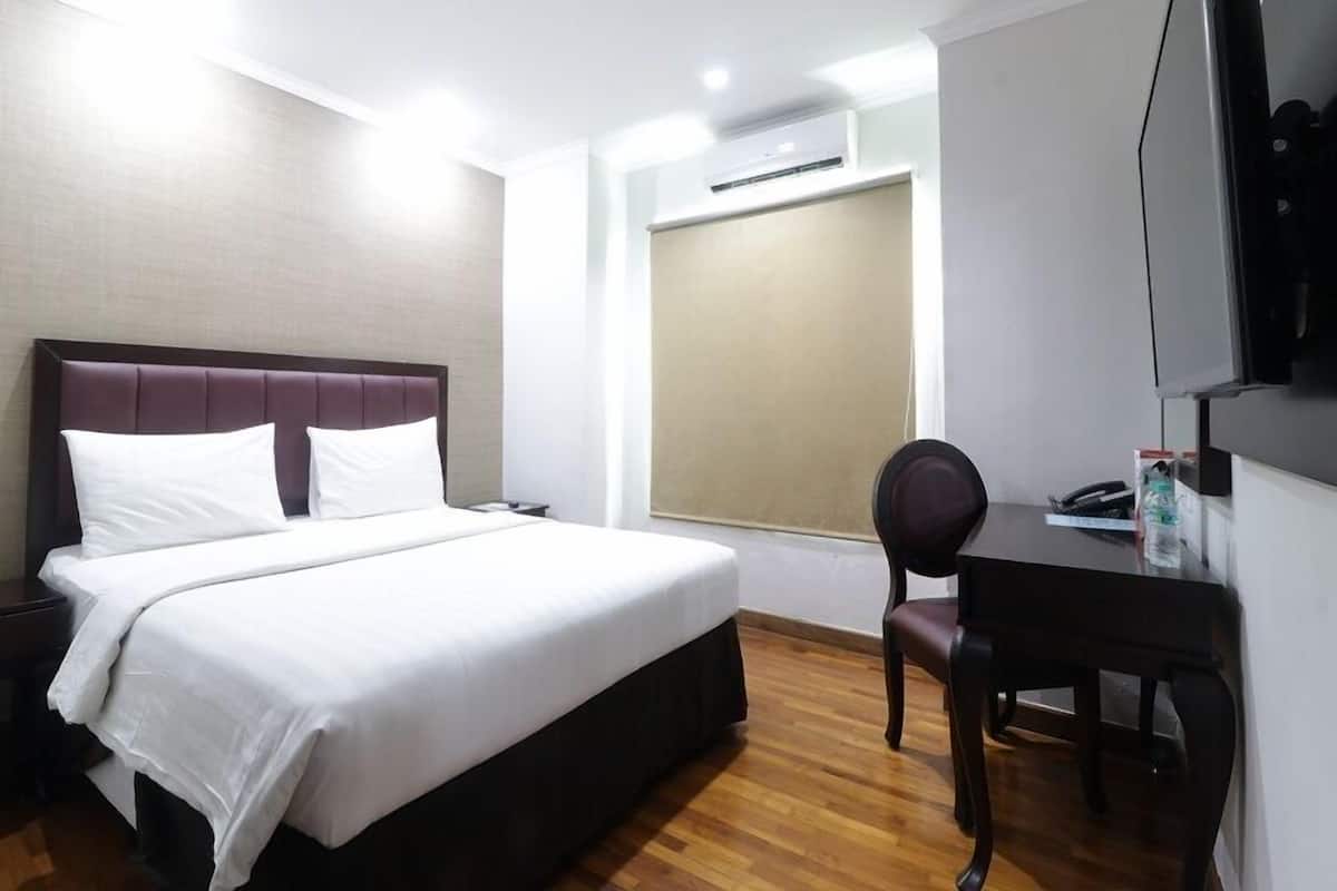 A hotel room with a bed, a desk, a chair, a TV, and an air conditioning unit.