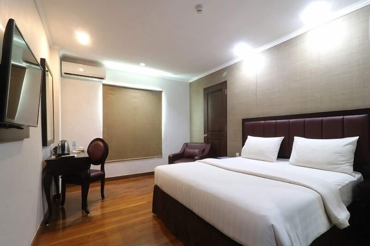 A hotel room with a large bed, a desk with a chair, a television, and a window with a blind.