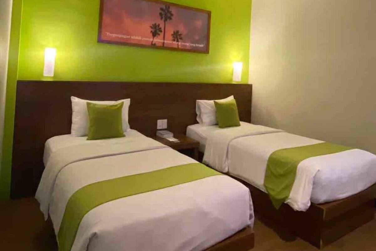 Une chambre d’hôtel avec deux lits, des murs verts, un tableau et des lampes de chevet.