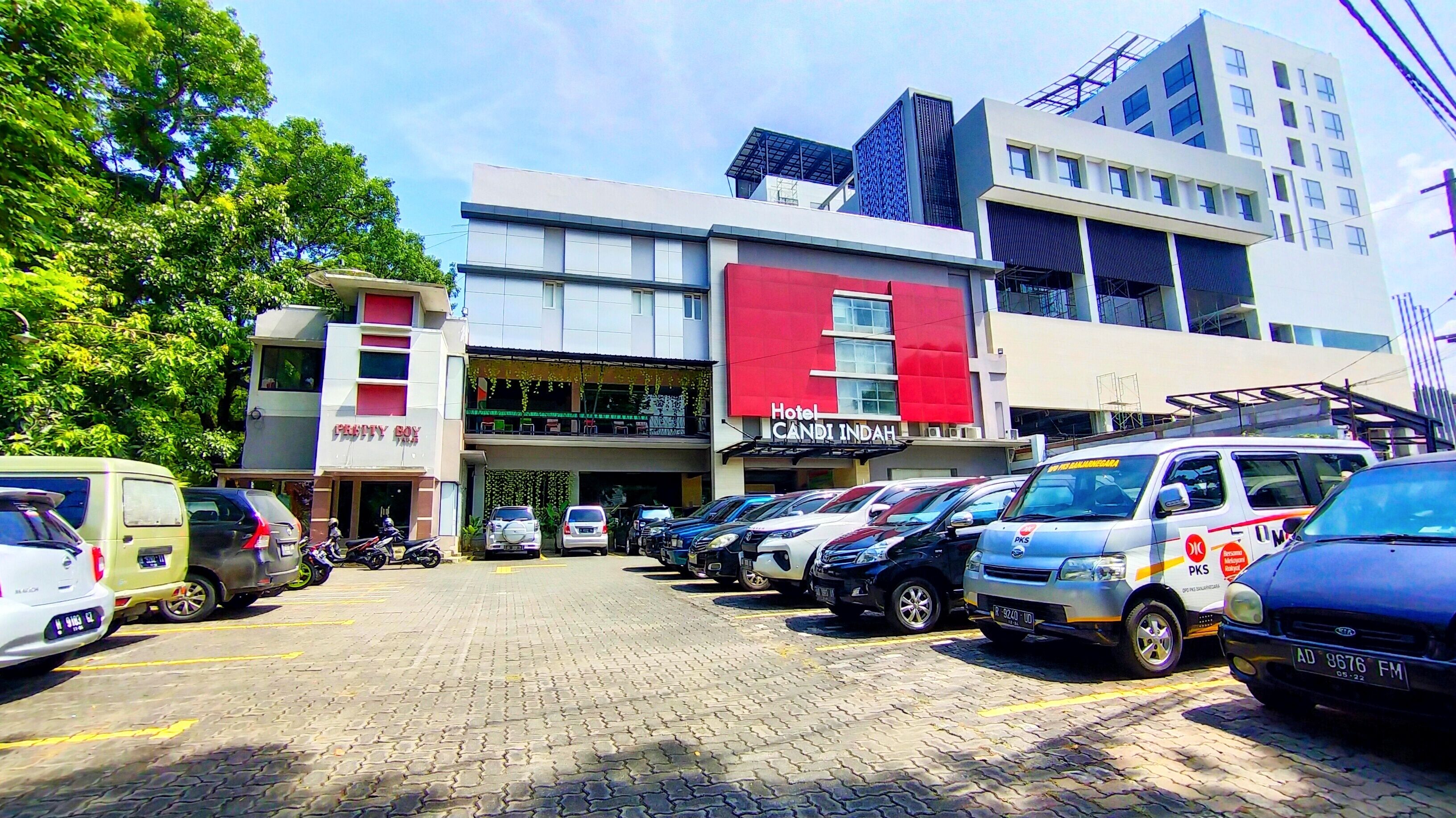 Un hotel de fachada roja, un estacionamiento con varios coches y un edificio de diseño moderno al fondo.