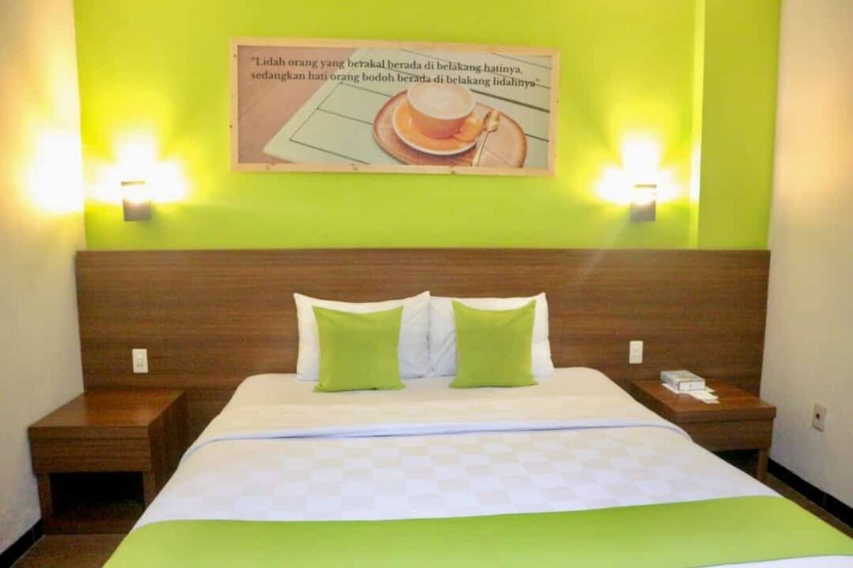 Une chambre d’hôtel avec un lit, deux tables de chevet, un mur vert et une affiche.