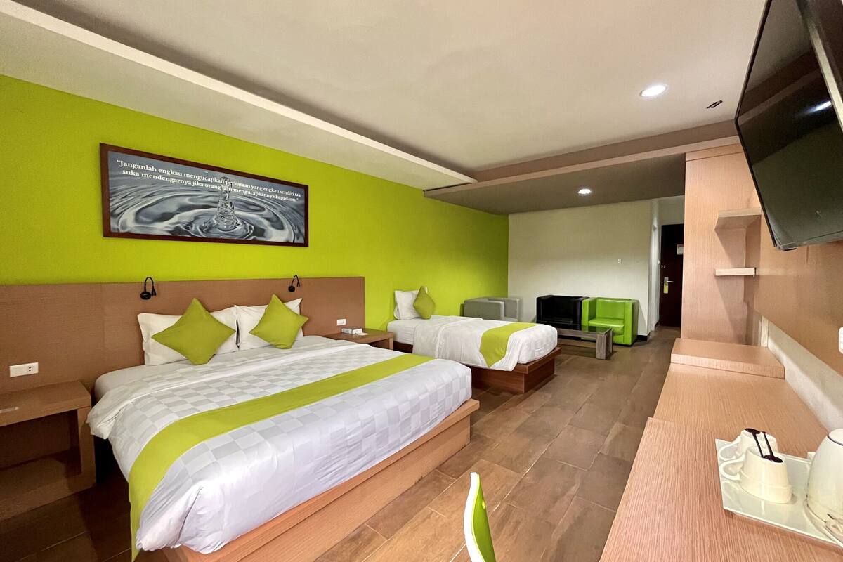 Une chambre d’hôtel avec deux lits, une télévision, un bureau équipé d’une cafetière et un mur vert orné d’une citation inspirante.