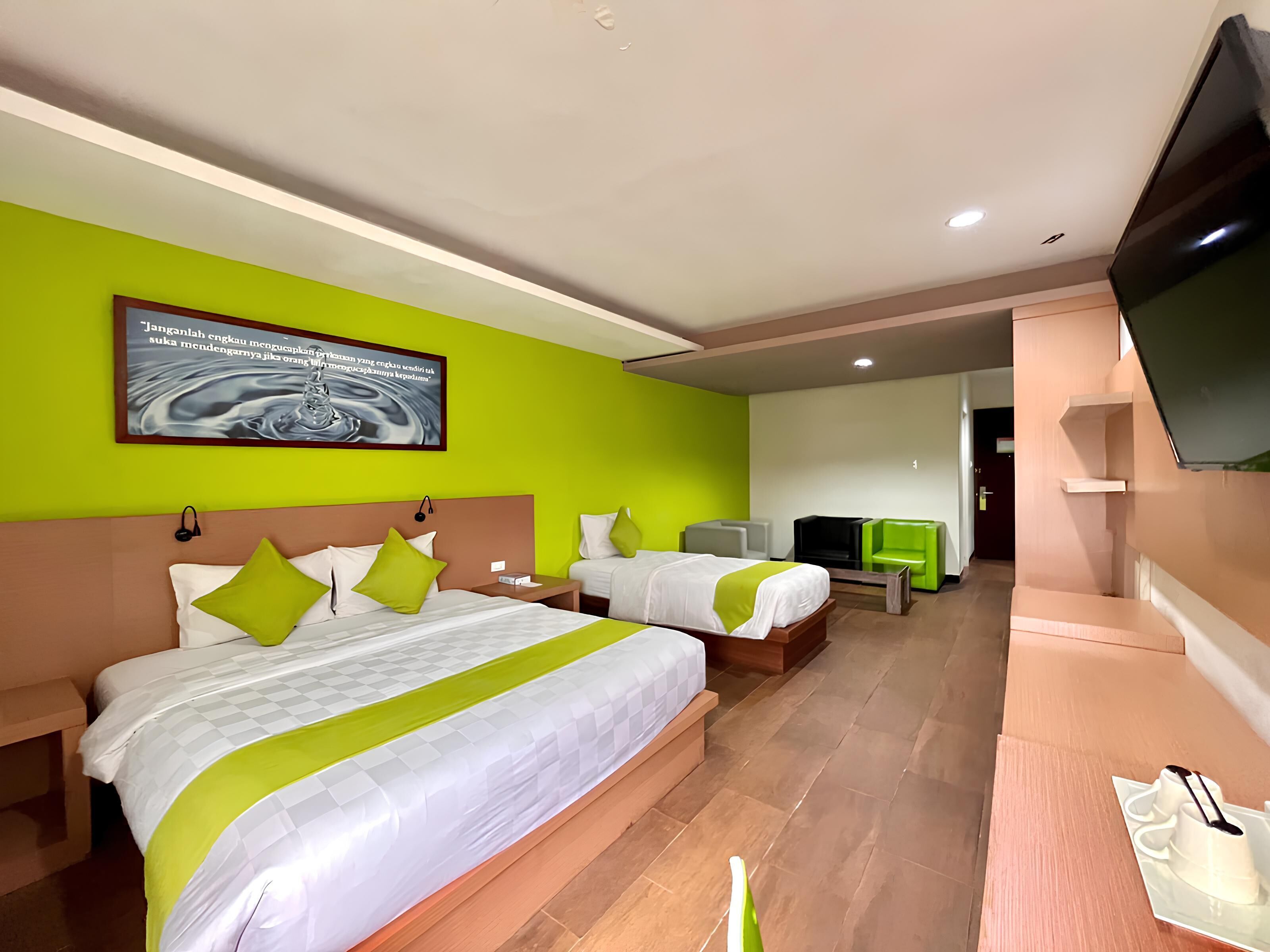 Habitación de hotel con dos camas, televisión, escritorio y pared verde.