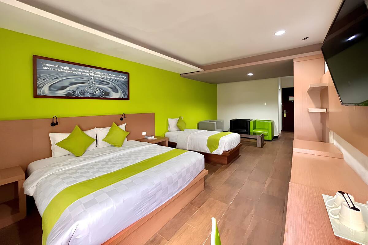 Une chambre d’hôtel avec deux lits, une télévision, un bureau et un mur vert.