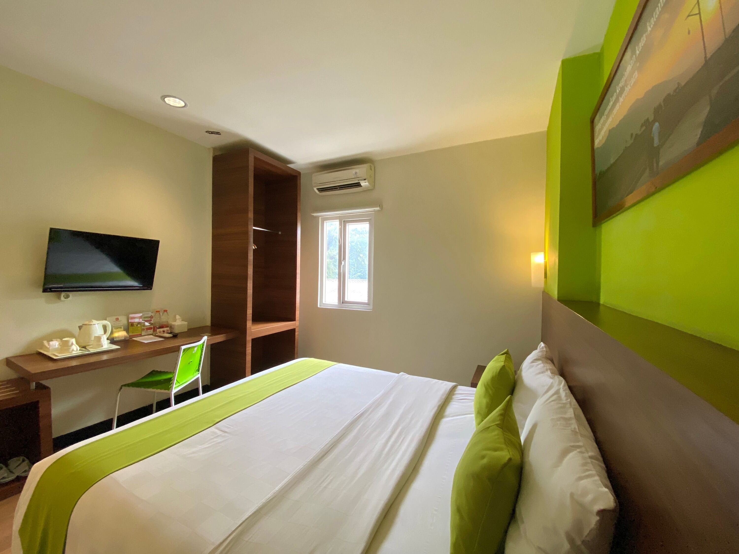 A hotel room with a bed, a desk with a chair, a television, and a window.
