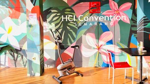 Una pared colorida con un gran mural de flores, una bicicleta estática y una mesa con una silla roja.