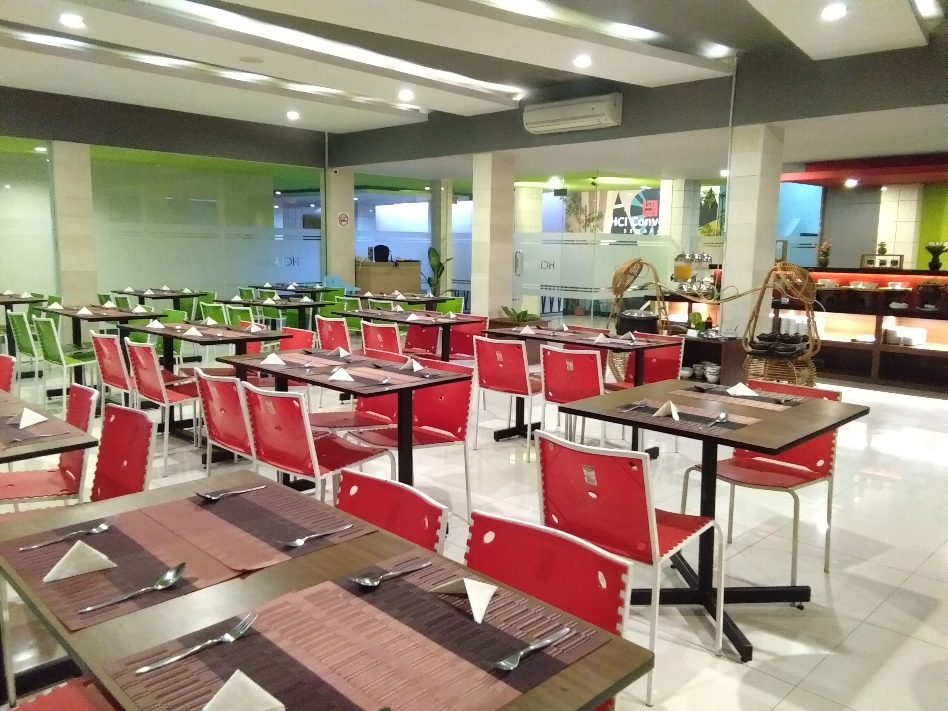 A dining area with multiple tables and chairs, a kitchen area in the background, and a green wall.