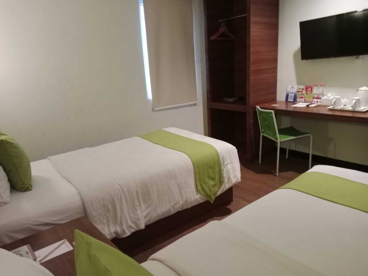 A hotel room with two beds, a desk with a chair, a TV, and a window.