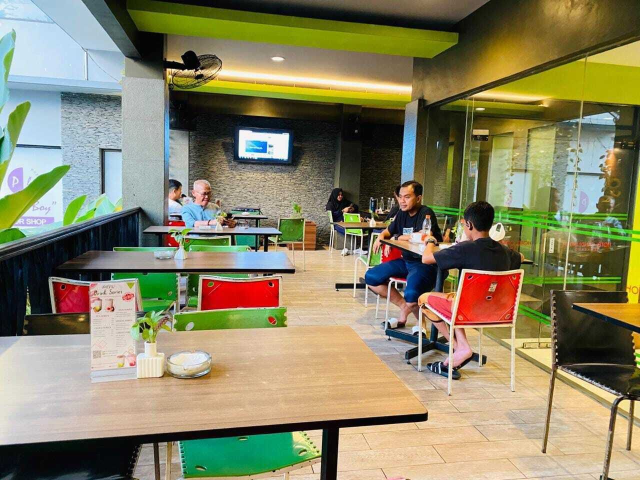 Una cafeteria moderna amb seients verd i vermell, una pantalla de televisió a la paret i un expositor de menús amb plats.
