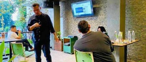 A modern indoor space with a green and grey color scheme, featuring a large screen on the wall, green chairs, and a casual seating area.
