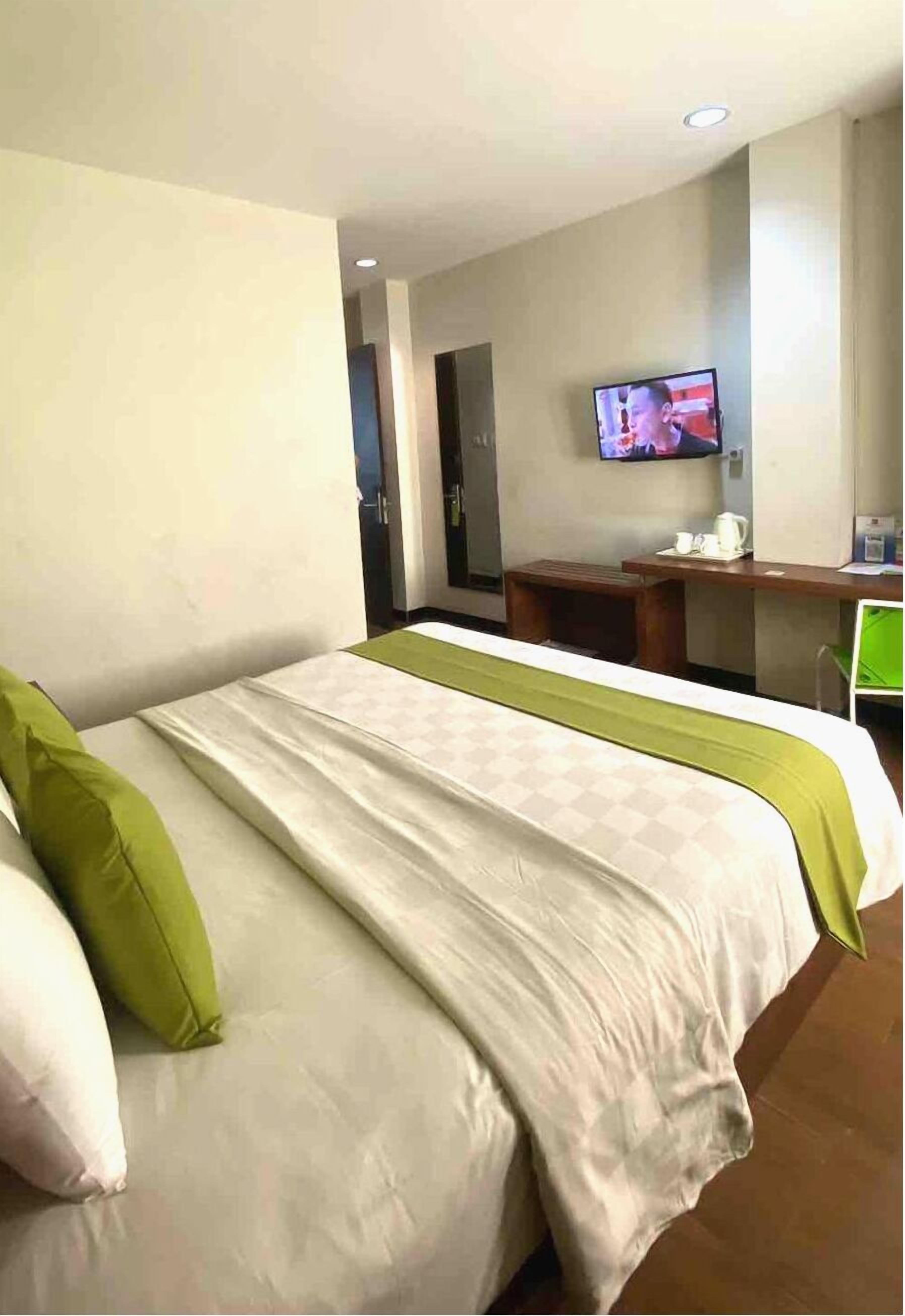 A hotel room with a bed, a desk, a television, and a door.
