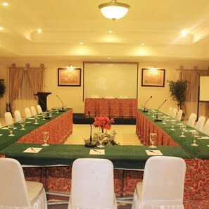A conference room with a long table, white chairs, a podium, and a large screen. - Resort Prima Coolibah Puncak (Cipanas)