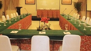 A conference room with a long table, white chairs, a podium, and a large screen. - Resort Prima Coolibah Puncak (Cipanas)