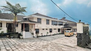 A two-story building with a restaurant and reception area, paved driveway, and parked vehicles. - Resort Prima Coolibah Puncak (Cipanas)