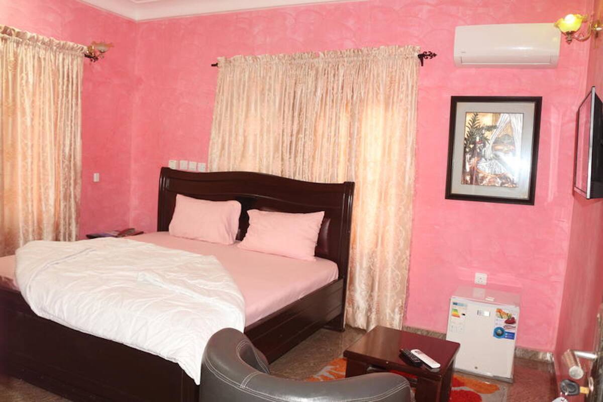 A bedroom with a bed, curtains, a TV, and a refrigerator.
