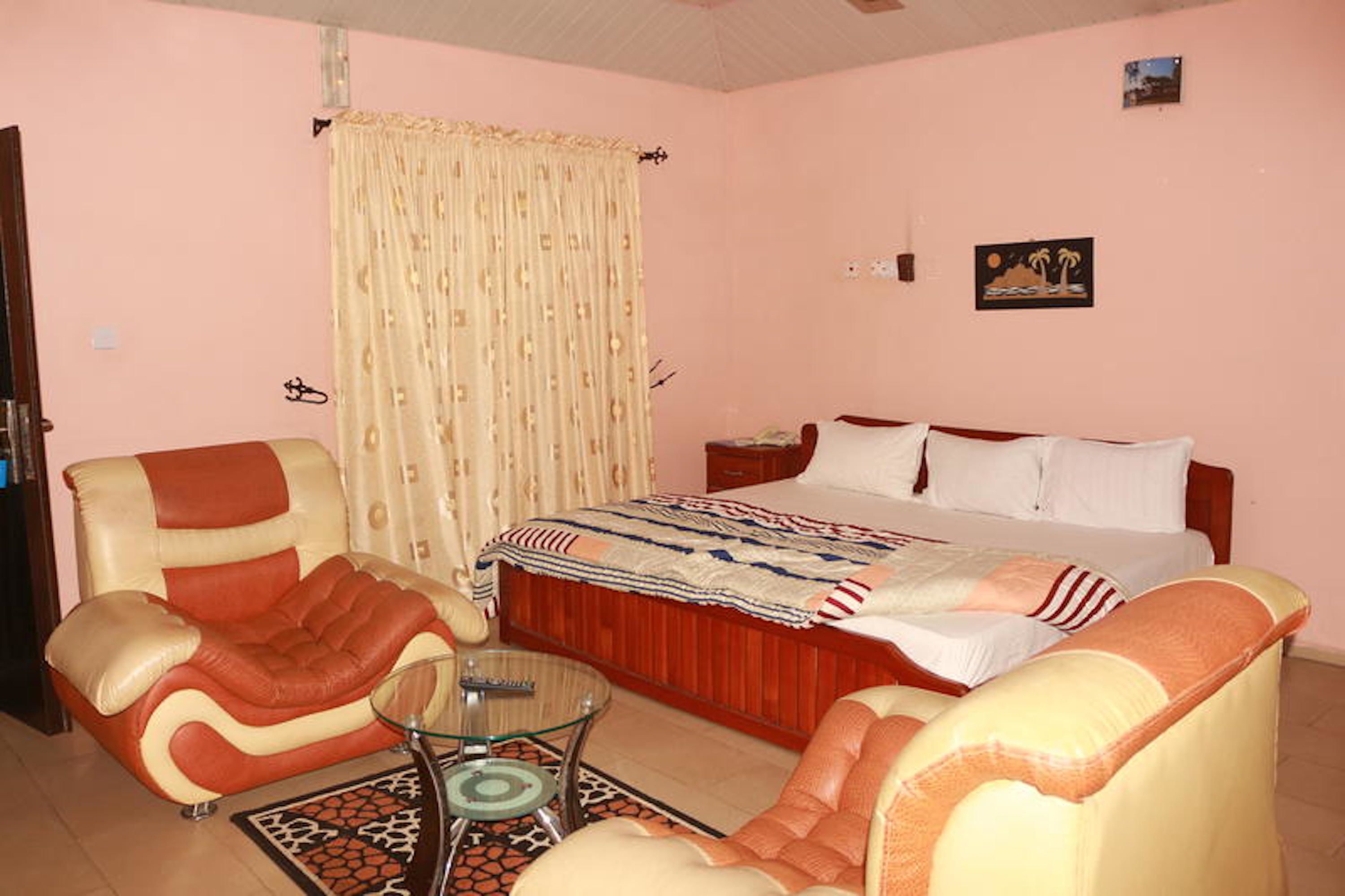 A bedroom with a bed, two armchairs, a small table, and a curtain.