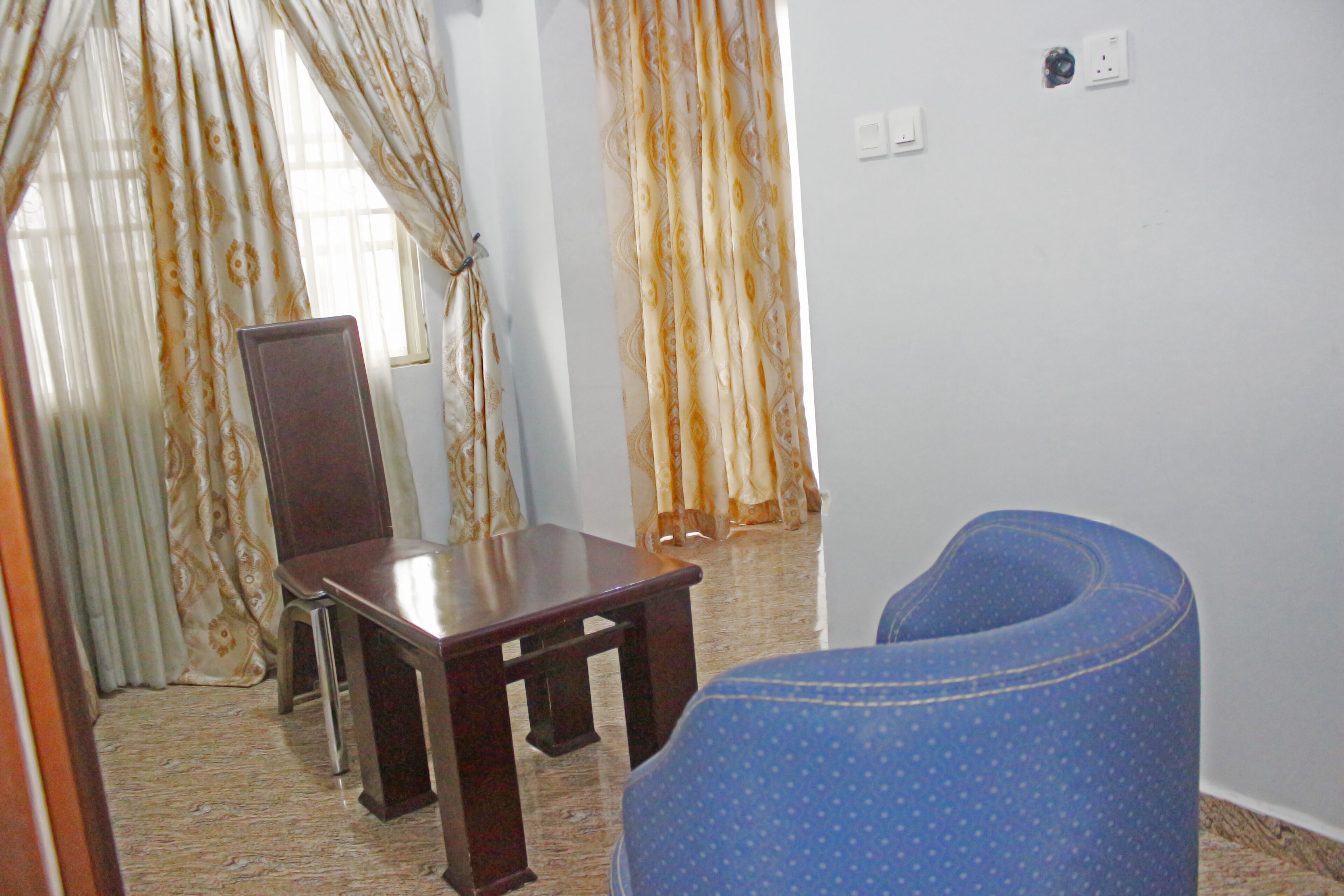 Una habitación con una mesa de madera, una silla azul y cortinas estampadas.