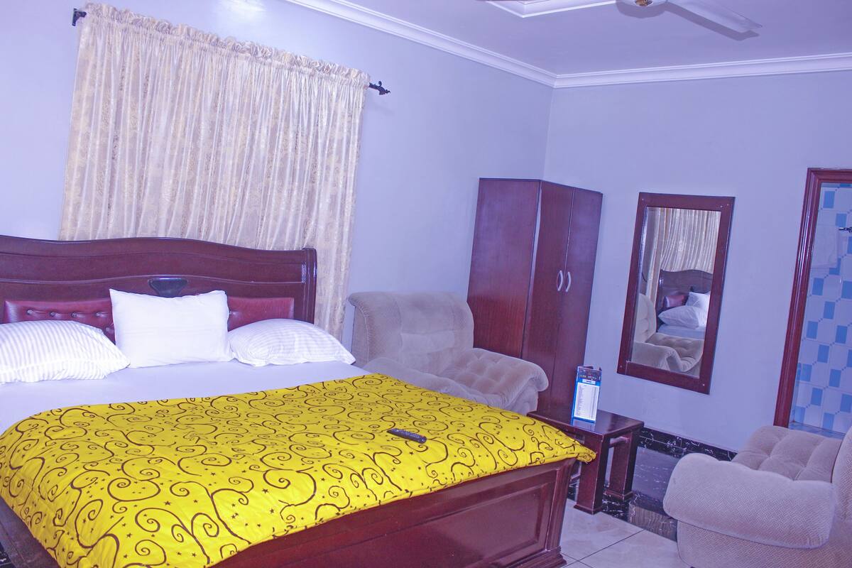 A bedroom with a bed, a chair, a wardrobe, and a mirror.