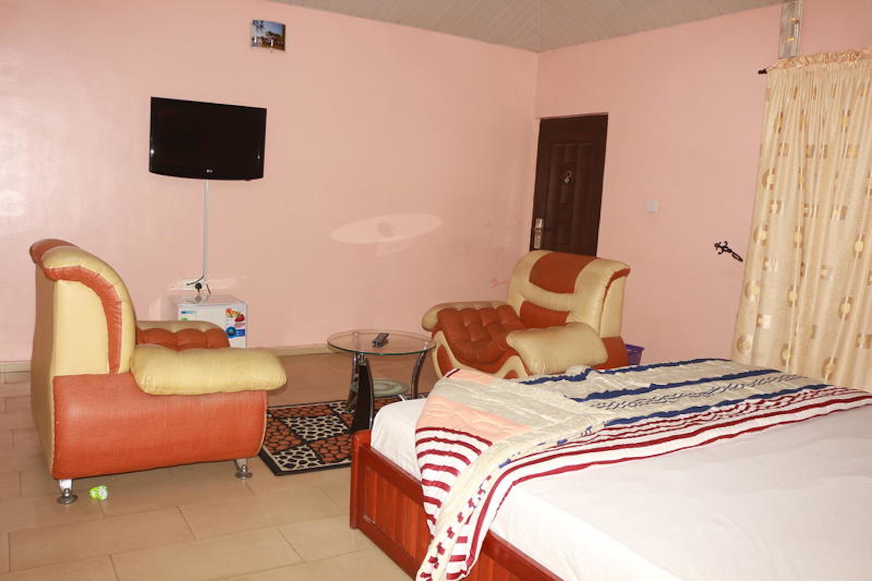 A hotel room with a bed, two armchairs, a small table, and a television on the wall.