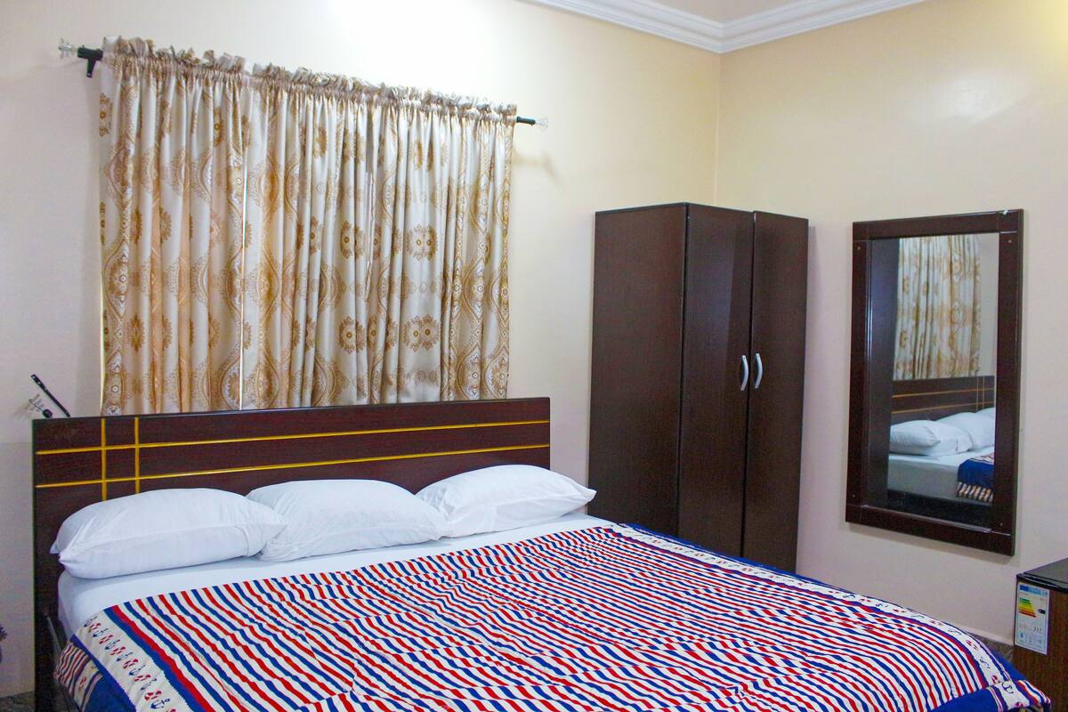 A neatly made bed with a patterned bedspread, a dark wooden wardrobe, and a mirror on the wall.