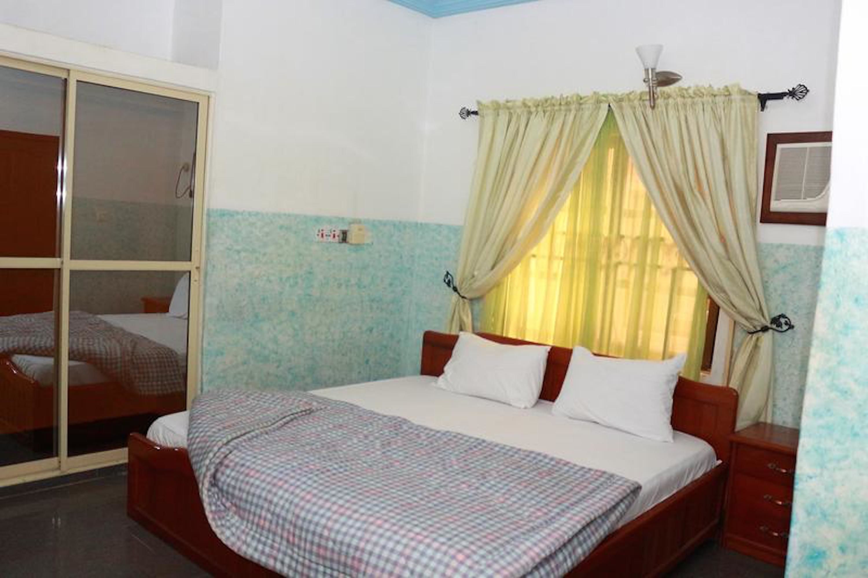 A bedroom with a bed, a wardrobe, and a window with curtains.