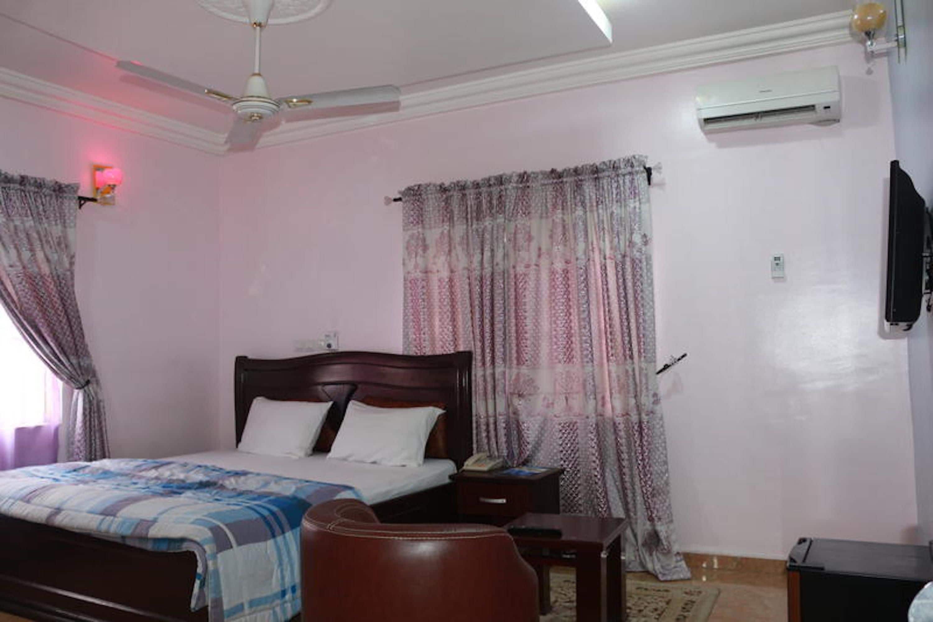 Een slaapkamer met een bed, een bureau, een stoel, een airconditioner en gordijnen.