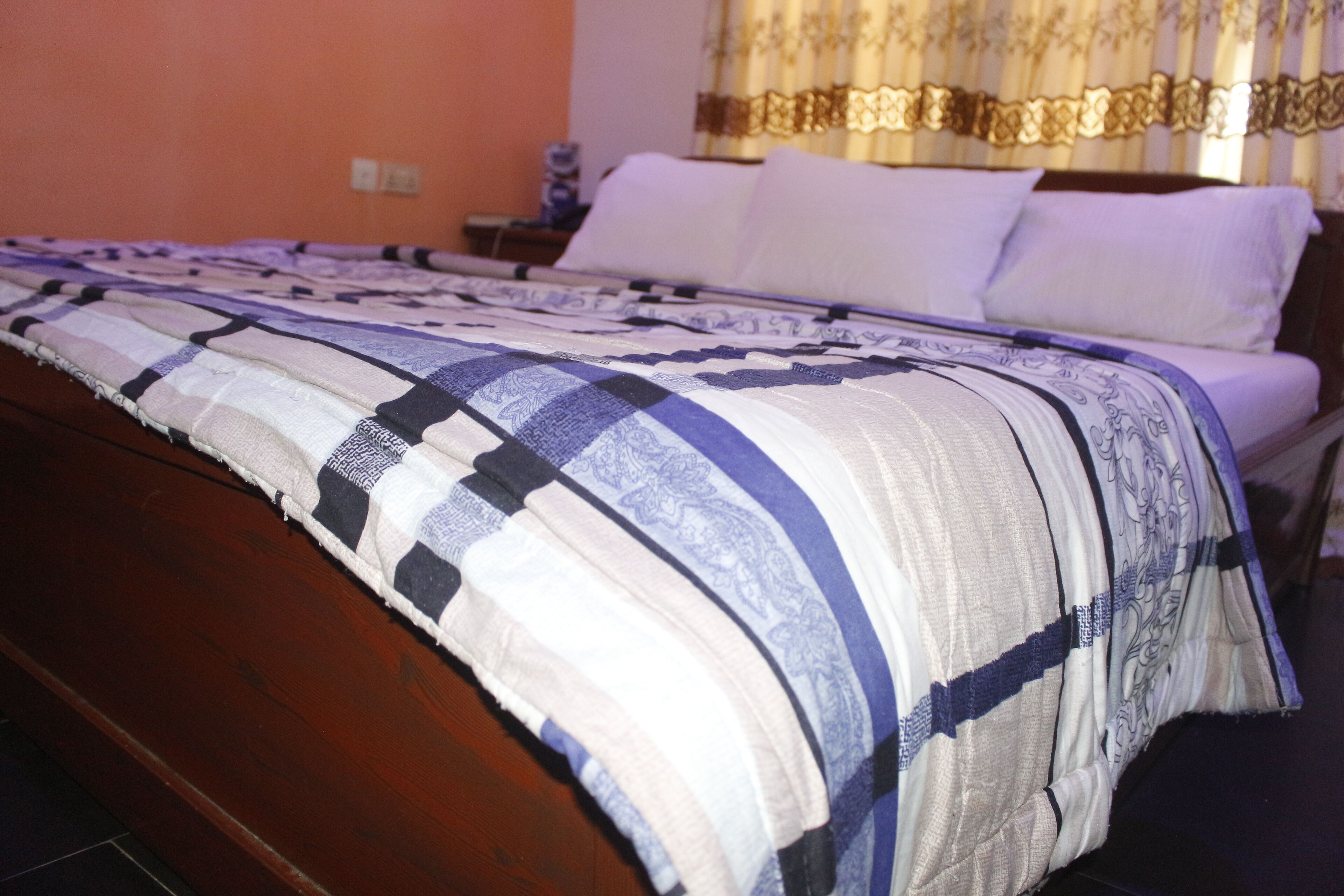 A bed with a patterned bedspread, a wooden headboard, and a nightstand with a lamp.