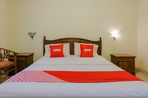 Un lit bien fait, recouvert d’une couette blanche et rouge, avec deux oreillers rouges portant le logo « OYO », et une tête de lit en bois.