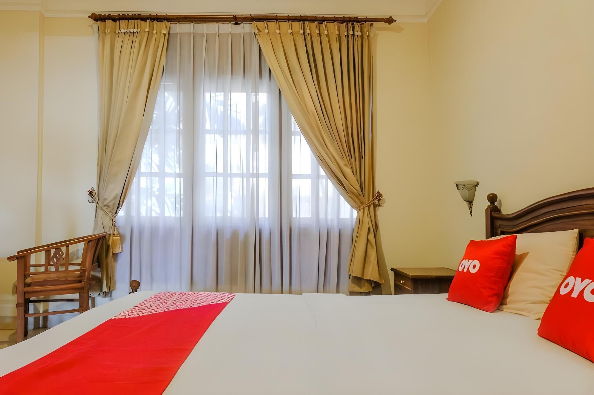 Une chambre d’hôtel avec un lit, des rideaux, une chaise en bois et une table de chevet.