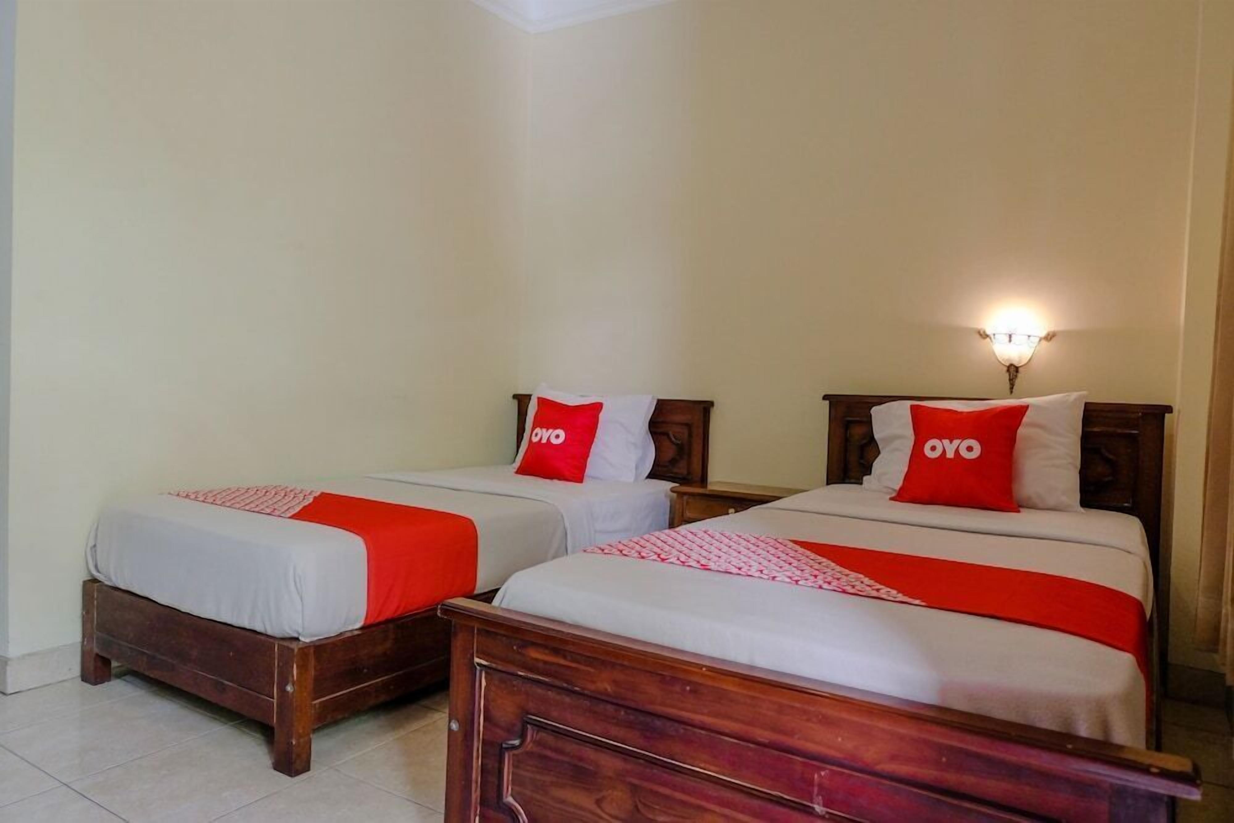 Two wooden beds with white bedding and red accents, including pillows with the word "OYO" on them.